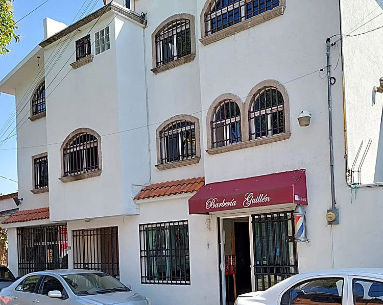 Fachada blanca con ventanas en arco de cantera; en la planta baja, el toldo guinda de Barbería Guillén y el poste de barbero junto a la puerta